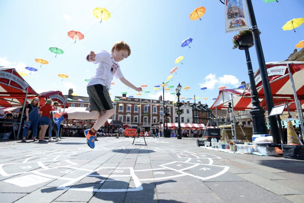 Young boy playing hopscotch in a town centre market place on a sunny day.